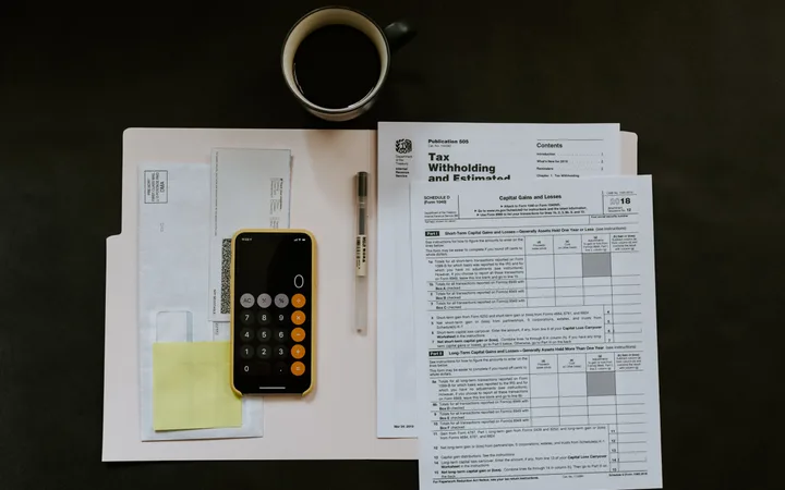 A top-down view of a workspace with a cup of coffee, financial documents, a calculator on a notepad, and a pen on a dark surface.