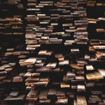 Stacked wooden planks forming a dense, layered arrangement with a dark background.