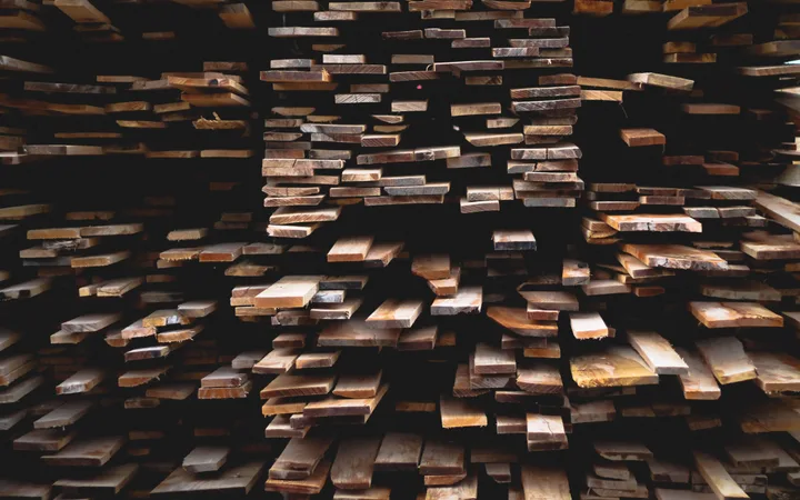 Stacked wooden planks arranged with dark gaps in between, creating an abstract textured surface with some light reflections.