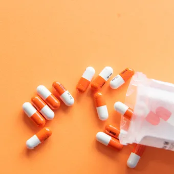 Orange and white capsules spilling from a partially open plastic bottle on an orange background.