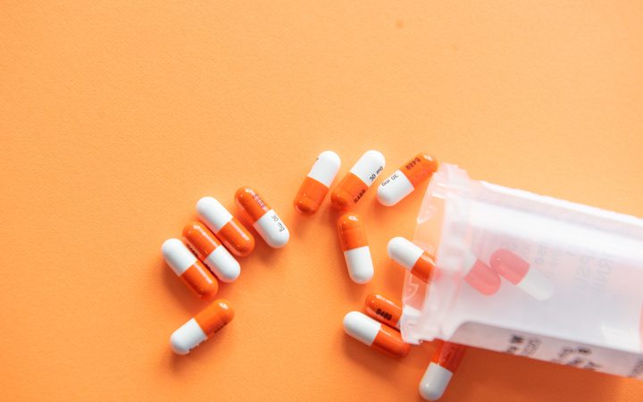 Orange and white capsules spilling from a partially open plastic bottle on an orange background.