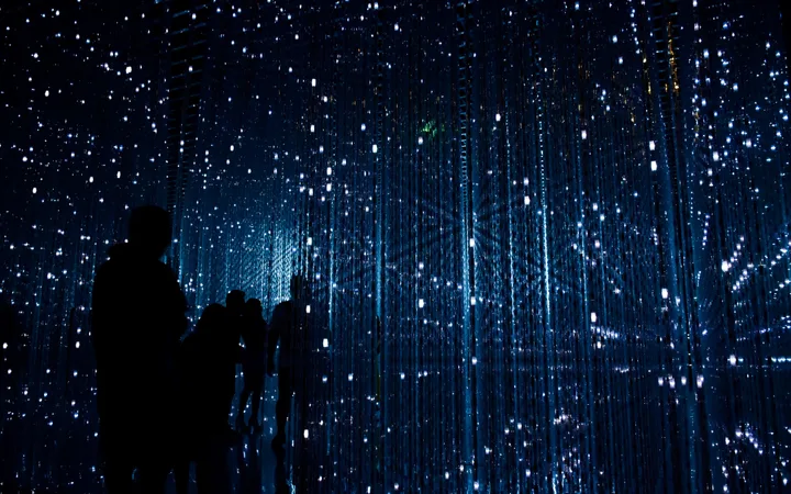 Silhouettes of people in a dark, starry-like tunnel with vertical strips of blue lights and shimmering reflections.