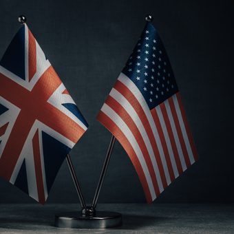 Small UK and US flags on a metal stand against a dark background.