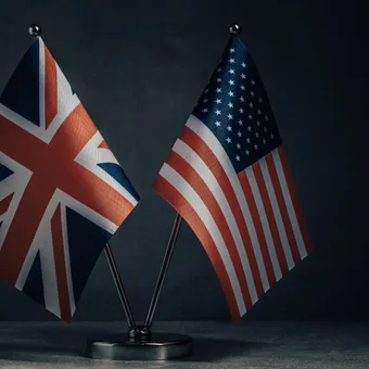 Small UK and US flags on a metal stand against a dark background.