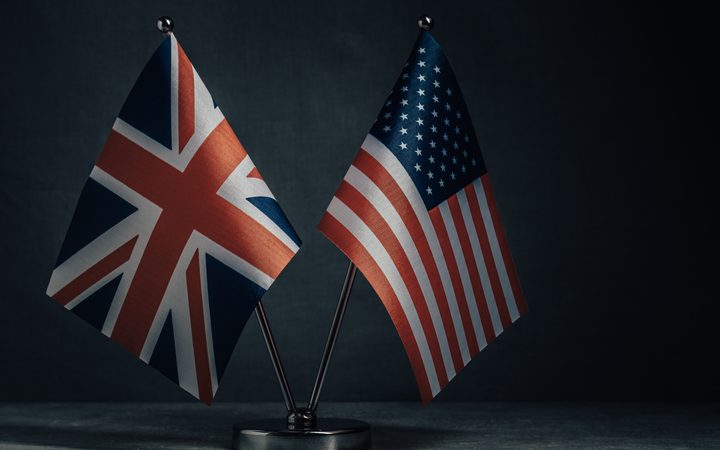Small UK and US flags on a metal stand against a dark background.