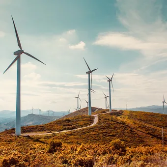 Wind turbines on a grassy hill under a partly cloudy sky with mountains in the background.