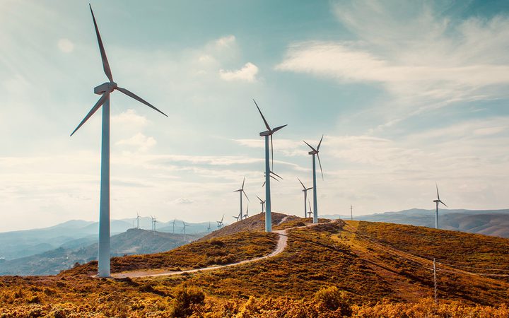Wind turbines on a grassy hill under a partly cloudy sky with mountains in the background.