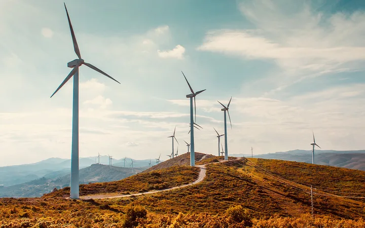 Wind turbines on a grassy hill under a partly cloudy sky with mountains in the background.