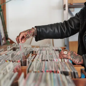 A person with a shaved head and light beard, wearing a blue striped shirt with a white collar, posing against a grey background.