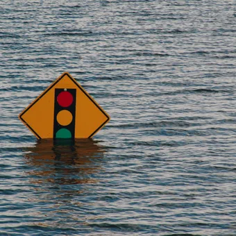 A traffic light sign partially submerged in water, floating on a calm body of water with ripples.