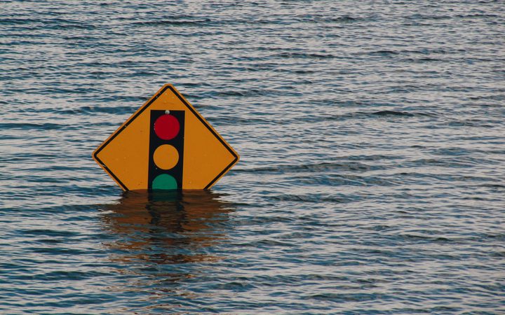 A brightly coloured traffic light warning sign is floating upright in calm water, with the focus mainly on the sign and water reflection.