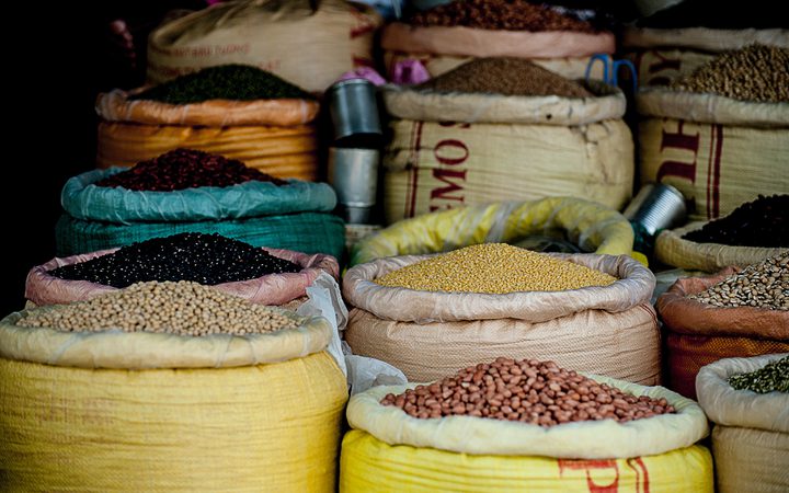Bags of various grains and legumes displayed at a market stall, with vibrant colors and textures filling the composition.