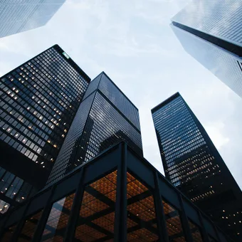 Low-angle view of tall modern glass skyscrapers against a cloudy sky.