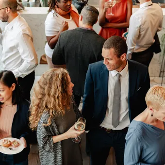 Porträt einer Person mit kurzen braunen Haaren, hellblauem Hemd, neutralem Gesichtsausdruck vor grauem Hintergrund.