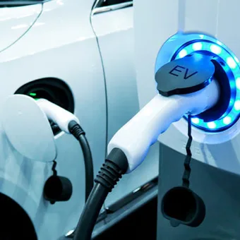 Electric vehicle being charged at a station with a glowing blue ring, hooked up to the car's charging port.