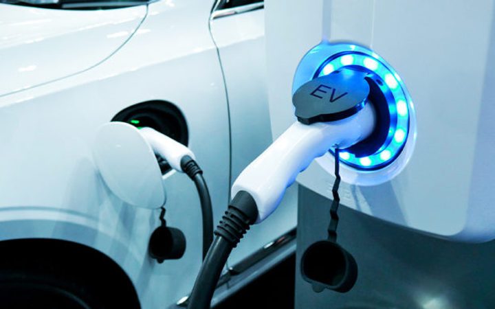 Electric vehicle being charged at a station with a glowing blue ring, hooked up to the car's charging port.