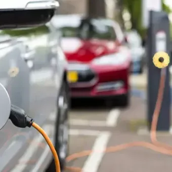 An electric vehicle charging at a station on a parking lot, with other cars and charging points visible in the background.