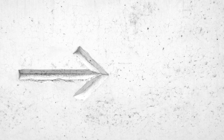 A worn, white wall with a rough texture and faint cracks, featuring a carved arrow pointing to the right.