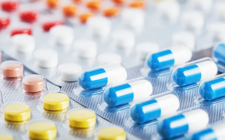 Blister packs of various pills in different shapes and colours, including yellow, pink, and blue and white capsules.