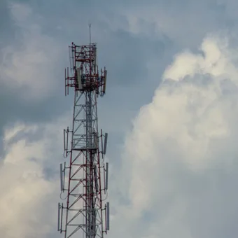 A tall communication tower with multiple antennas against a cloudy sky.