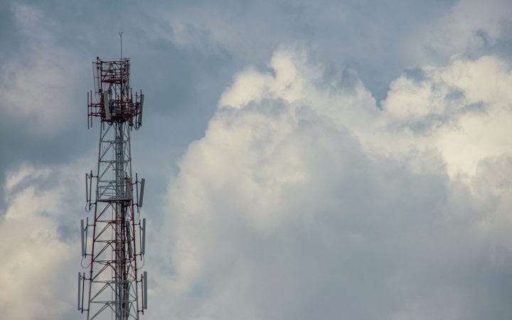 A tall communication tower with multiple antennas against a cloudy sky.