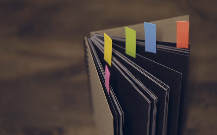 Open notebook with colorful sticky notes inserted between the pages, placed on a wooden surface.