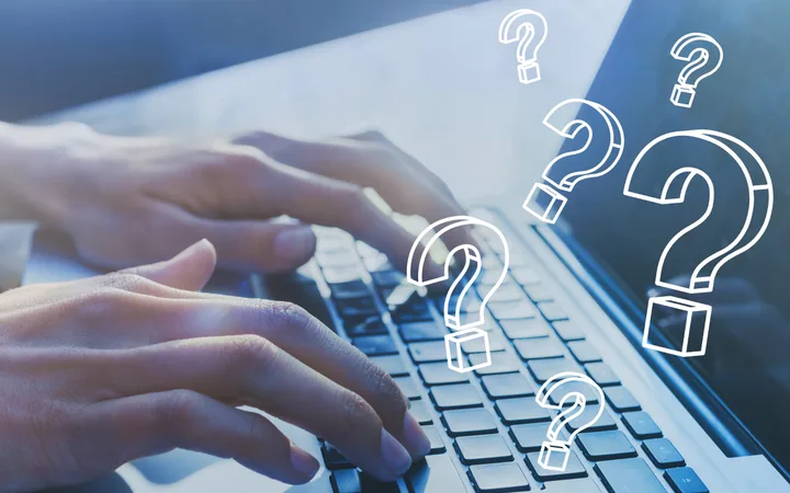 Hands typing on a laptop keyboard with floating question marks above, suggesting confusion or inquiry.