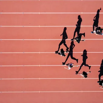 People jogging on a red outdoor track, casting long shadows, with white lane lines and a reddish pink background.
