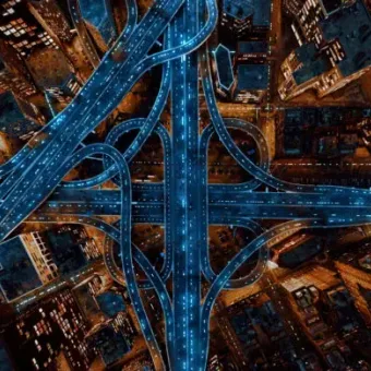 Aerial view of a cityscape at night with illuminated highways and skyscrapers, showcasing a complex network of roads and tall buildings.