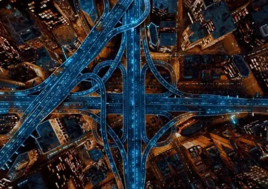 Aerial view of a city at night with illuminated highways and tall buildings surrounding the complex road network.