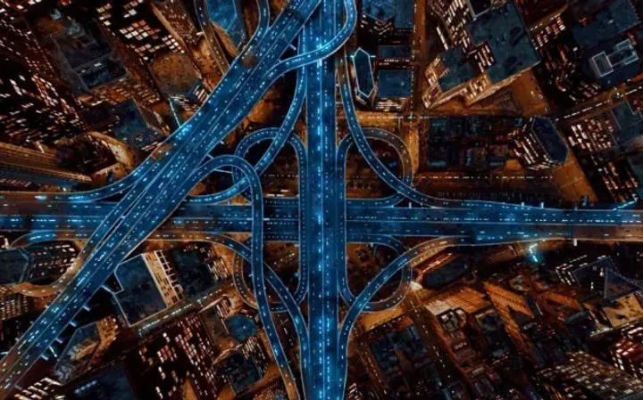 Aerial view of a cityscape at night with illuminated highways and skyscrapers, showcasing a complex network of roads and tall buildings.