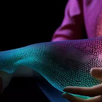 Person holding a holographic, colorful digital arm with a black background, highlighting advanced technology and human-computer interaction.
