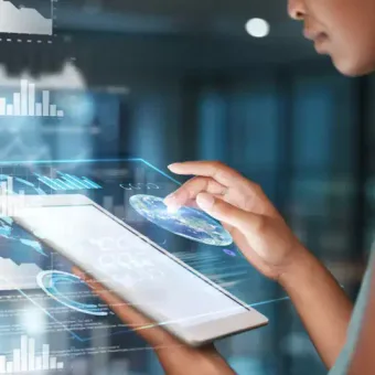 Person interacts with a transparent, holographic touch screen displaying graphs, charts, and digital data in a modern, high-tech environment.