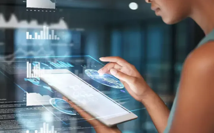 Person interacts with a transparent, holographic touch screen displaying graphs, charts, and digital data in a modern, high-tech environment.