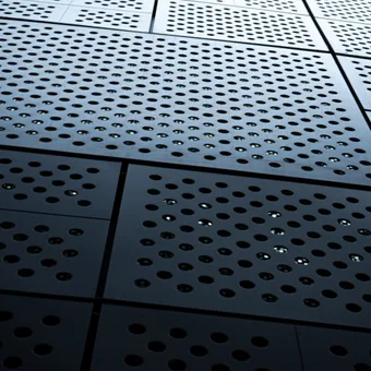 Close-up of a metallic perforated surface with circular holes arranged in grids, creating a pattern with reflections and shadows.