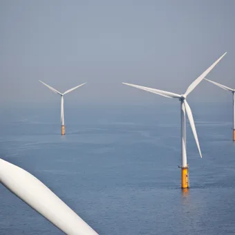 Offshore wind turbines in the sea, with a cloudy sky background, showing multiple turbines with white blades and orange bases.