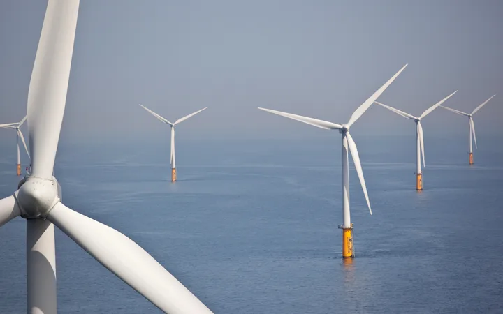 Offshore wind turbines in the sea, with a cloudy sky background, showing multiple turbines with white blades and orange bases.
