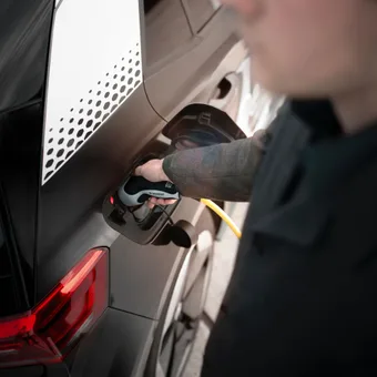 Person charging an electric vehicle with a charging gun connected to the car's charging port on the rear side.