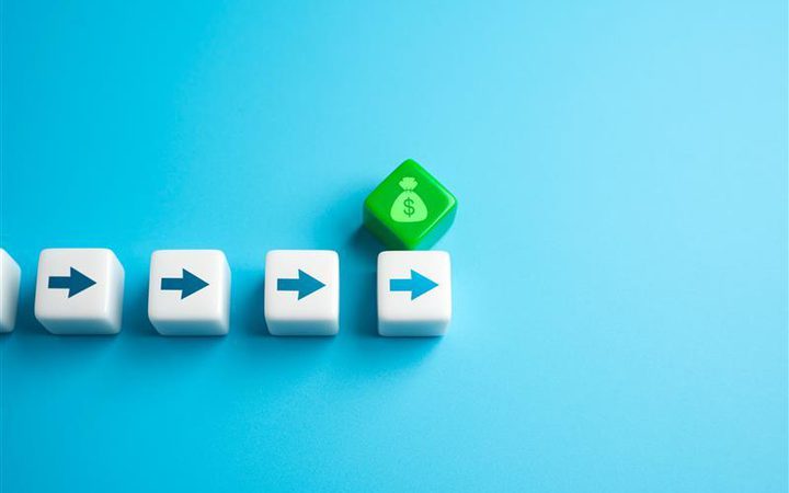 Four white dice with blue arrows pointing right, with a green dice featuring a money bag with a dollar sign on a blue background.