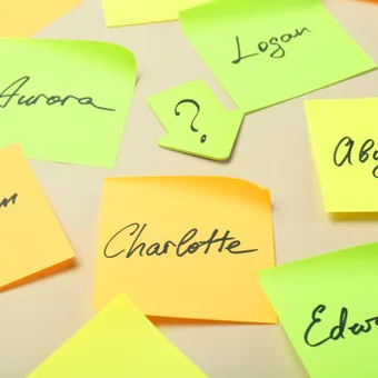 Neon sticky notes scattered on a beige surface with handwritten names such as Aurora, Logan, Abigail, Charlotte, Edward and William.
