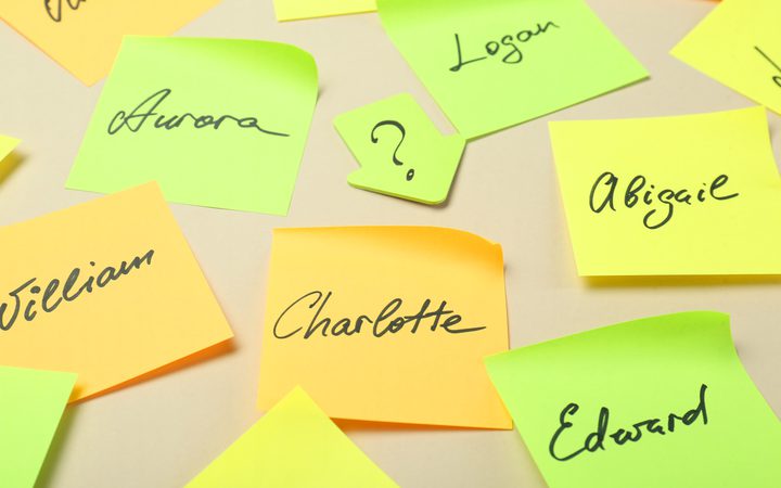 Neon sticky notes scattered on a beige surface with handwritten names such as Aurora, Logan, Abigail, Charlotte, Edward and William.