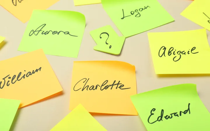 Neon sticky notes scattered on a beige surface with handwritten names such as Aurora, Logan, Abigail, Charlotte, Edward and William.