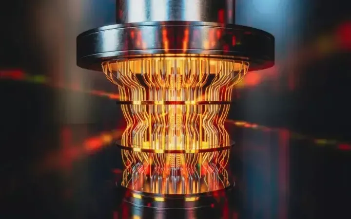 A close-up of a futuristic, glowing, orange and yellow circuit-like device, reflecting on a glossy dark surface, with a blurred background.