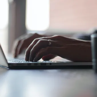 Person typing on a laptop keyboard with a focus on their hands and a blurred background.