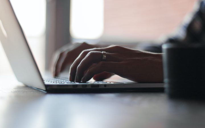 Person typing on a laptop keyboard with a focus on their hands and a blurred background.