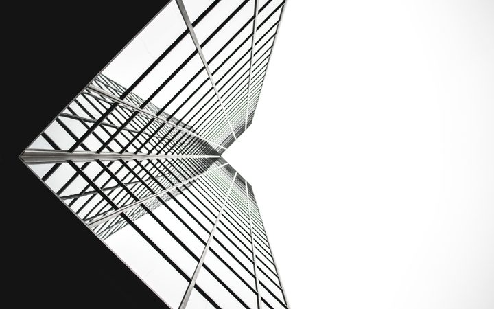 Looking up at a modern glass skyscraper with a grid-like pattern, the building's reflective surface contrasts with the plain white and black sky.