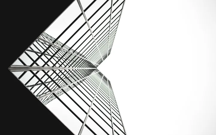 Looking up at a modern skyscraper with reflective glass windows, structural lines, and a stark contrast between the dark and white sections.