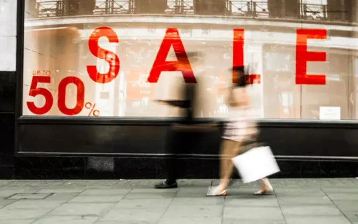 Blurred pedestrians walking past a store window with a large red "SALE" sign.