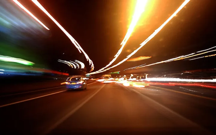 Bright streaks of light from moving cars and streetlights on a busy road at night, creating a dynamic, abstract scene.