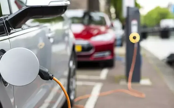 Electric vehicle charging station with a car plugged in, and other parking spaces and cars in the background.